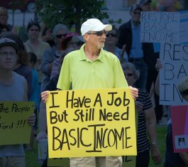 Man holding sign that says: I have a job but still need Basic Income