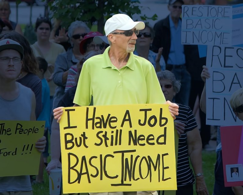 Man holding up sign that reads: I have a job but still Basic Income