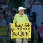 Man holding sign that says: I have a job but still need Basic Income